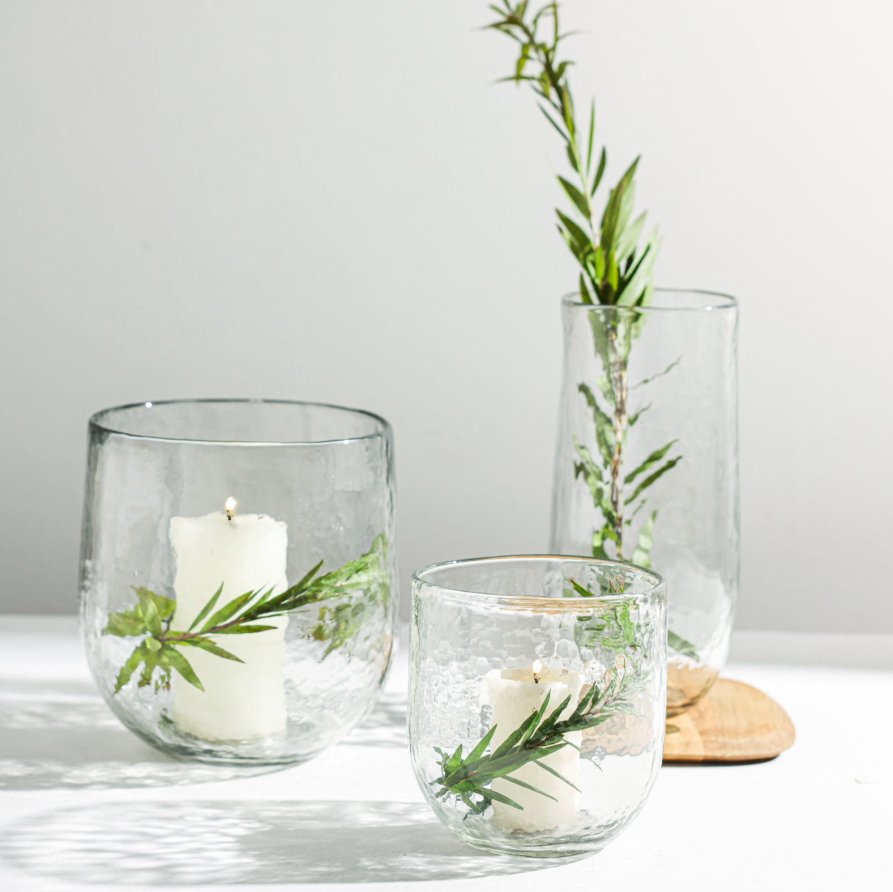 Clear glass containers with candles and greenery on a light surface