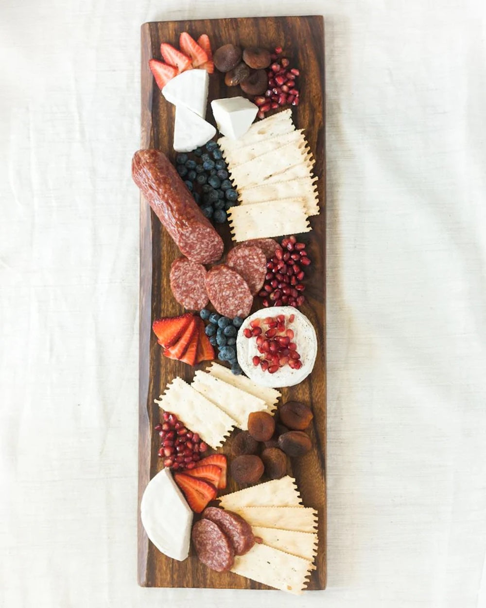 Wooden charcuterie board with various meats, cheeses, and fruits on a white background
