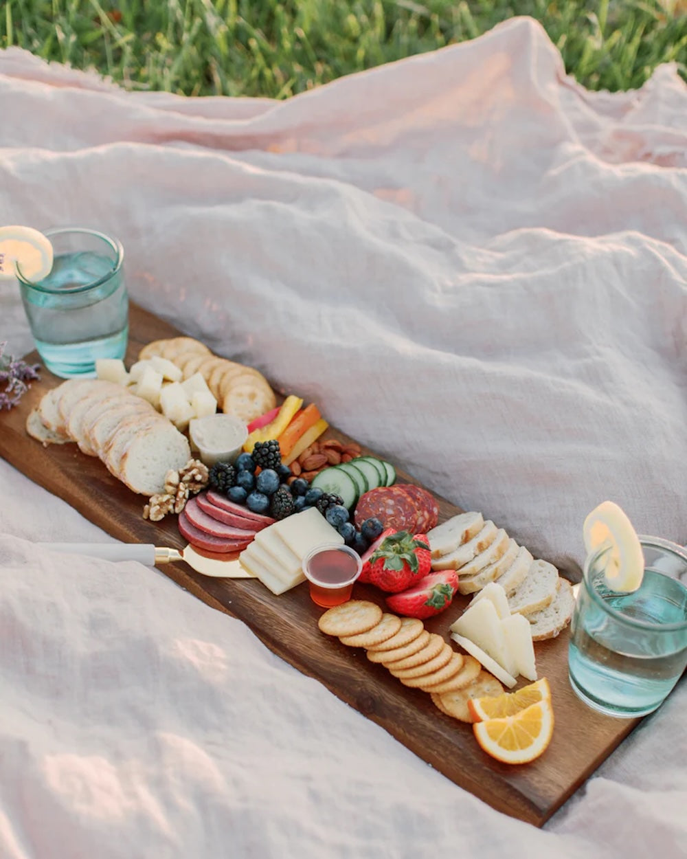 Picnic setup with a charcuterie board and drinks on a blanket outdoors.