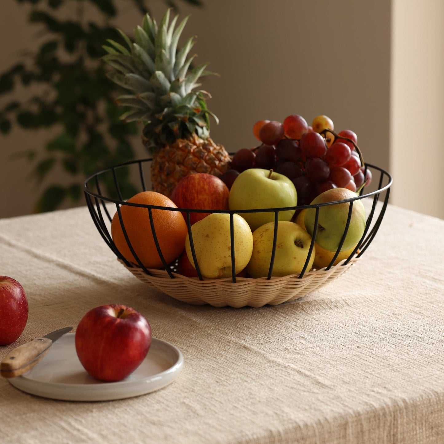 Fruit bowl with apples, oranges, and a pineapple on a table with a beige background