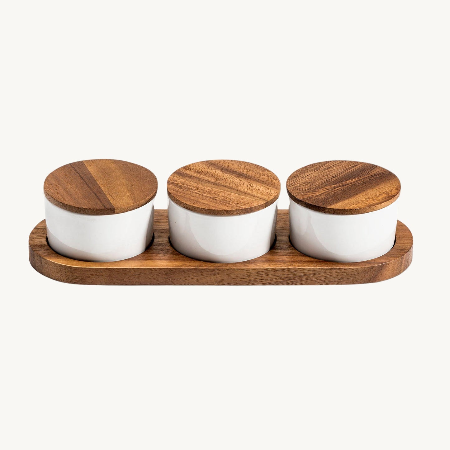 Set of three white jars with wooden lids on a wooden tray against a white background