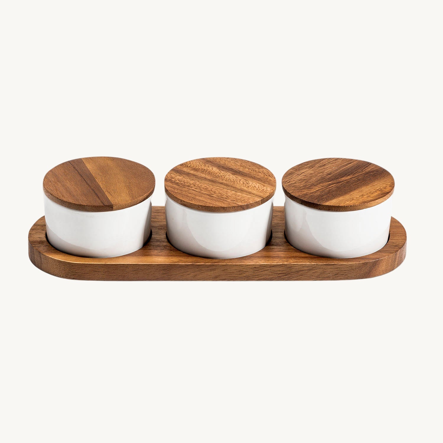 Set of three white jars with wooden lids on a wooden tray against a white background