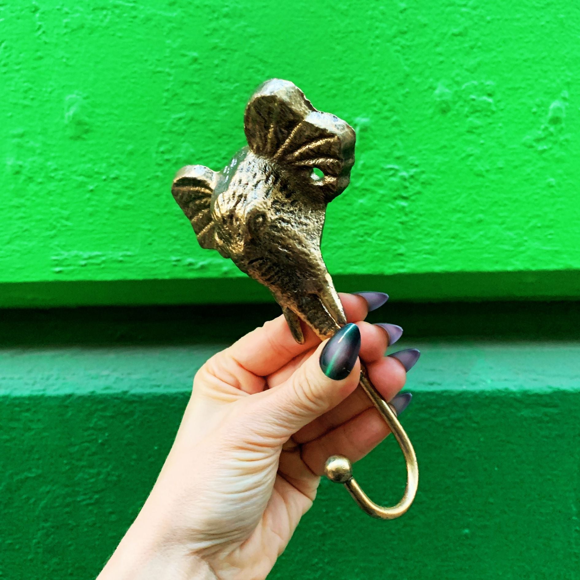 Hand holding a decorative brass hook against a green background