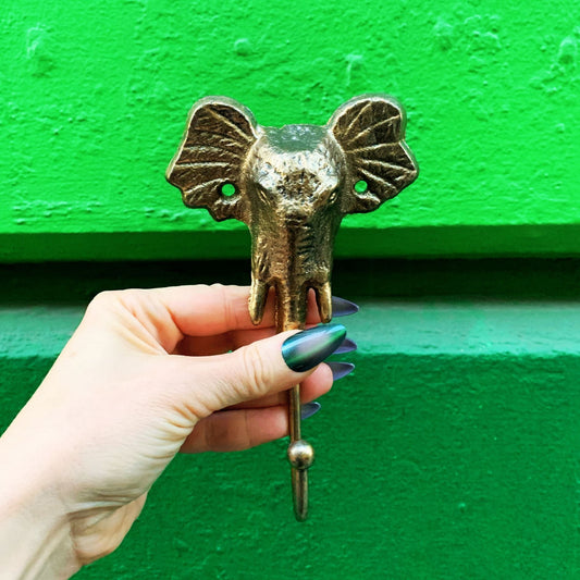Hand holding a brass elephant head hook against a green background