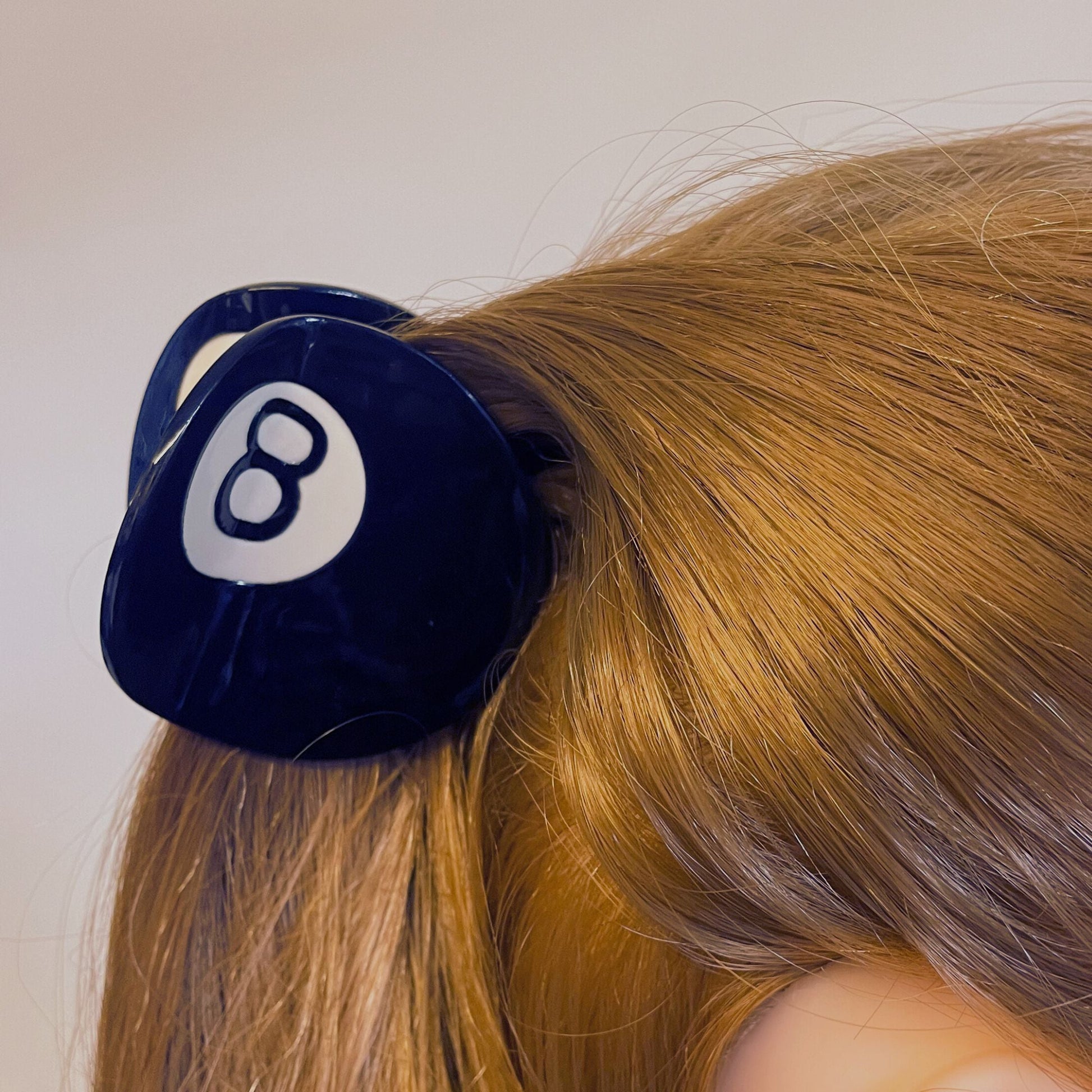 Black billiard ball hair clip with number 8 on a person's head against a neutral background
