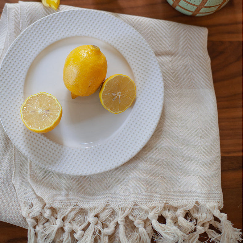 Three lemons on a white plate with a mug of coffee and yellow tulips in the background.
