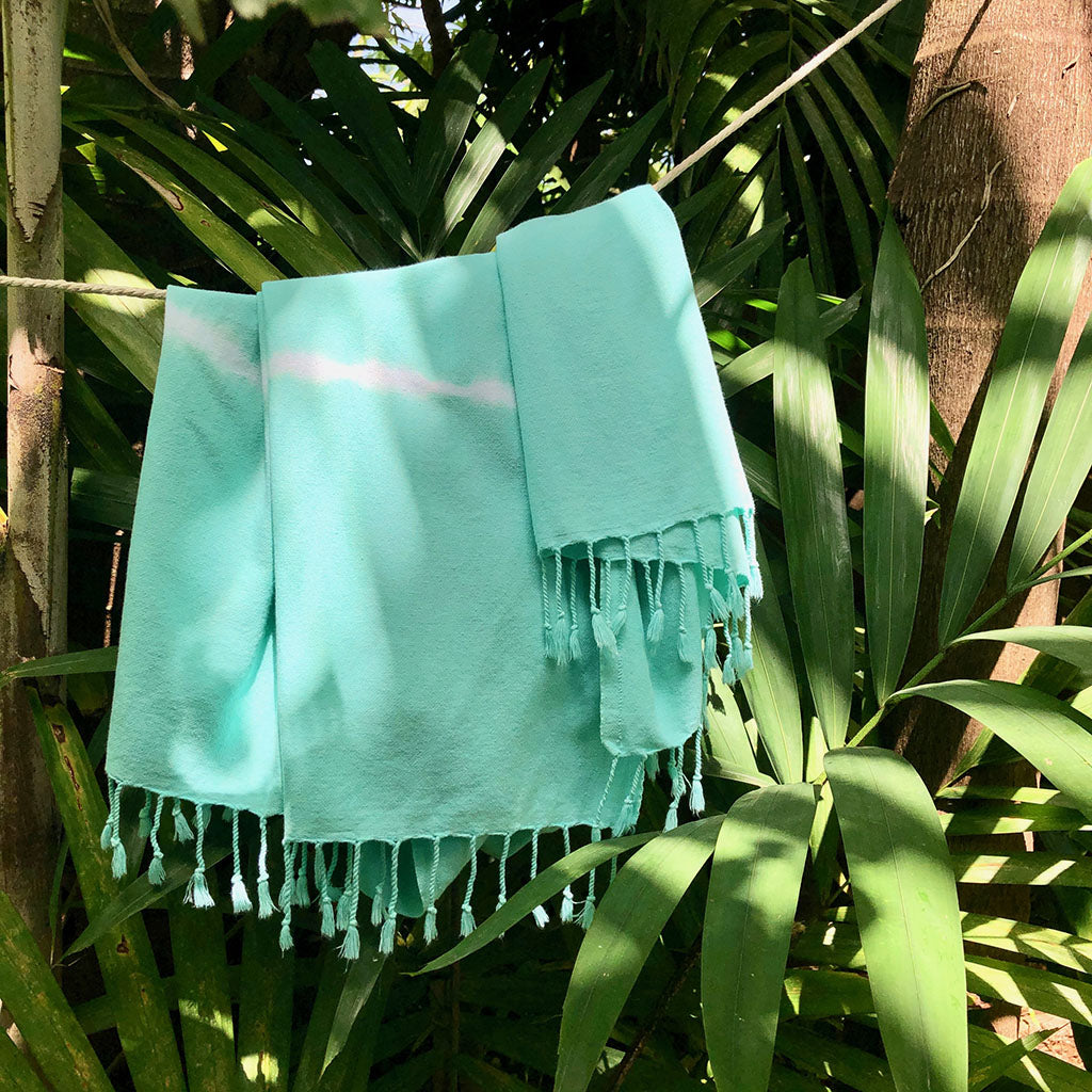 Turquoise towel with tassels hanging on a line surrounded by green foliage