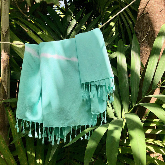 Turquoise towel with tassels hanging on a line surrounded by green foliage