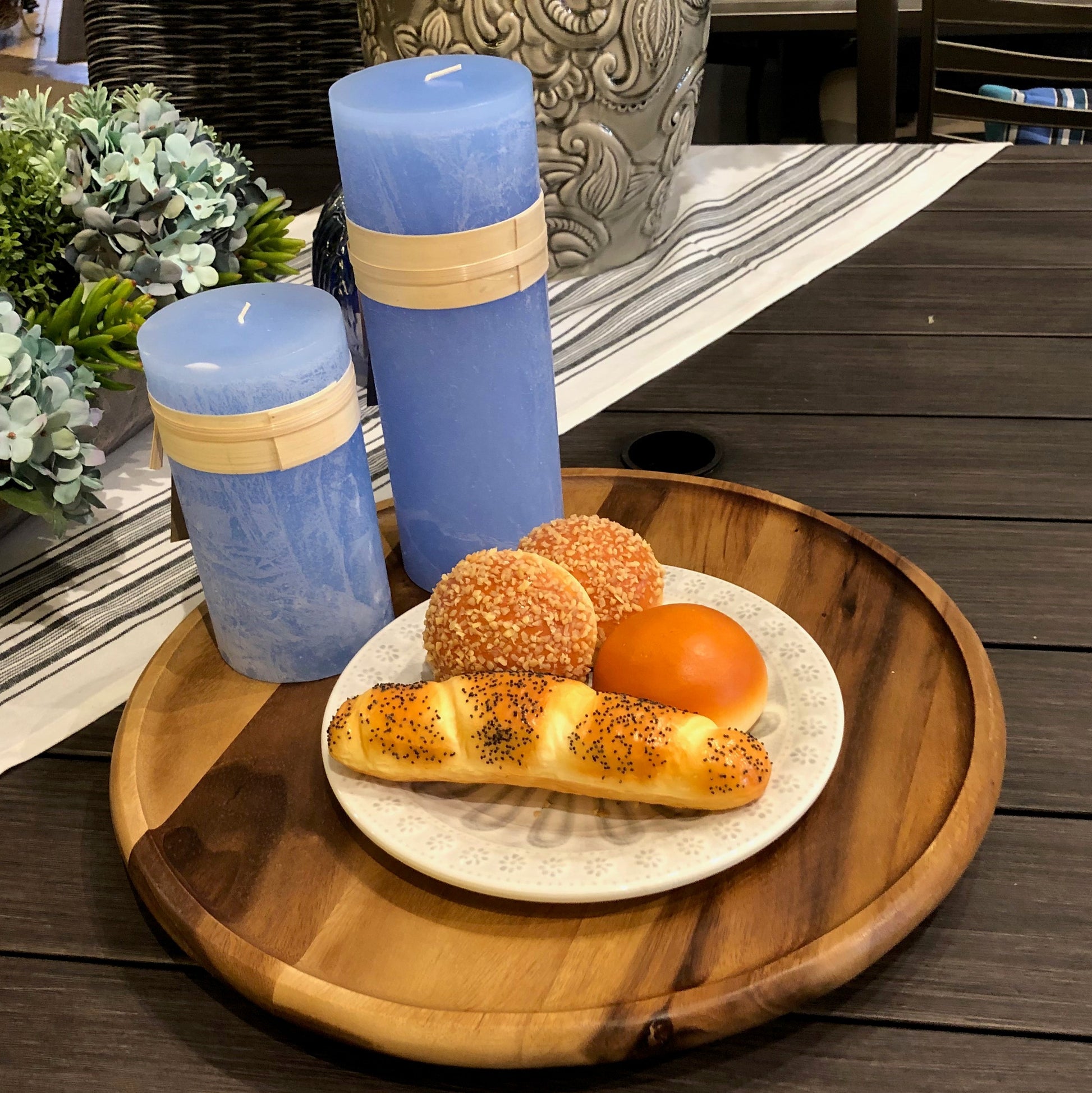 Three blue candles with wooden accents on a wooden tray with a plate of bread and pastries.