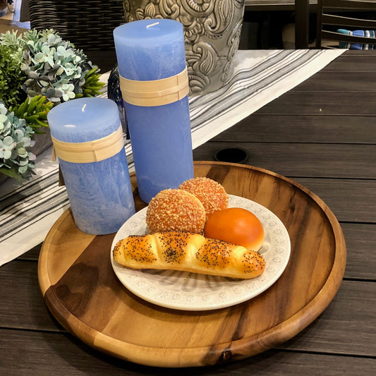 Three blue candles with wooden accents on a wooden tray with a plate of bread and pastries.