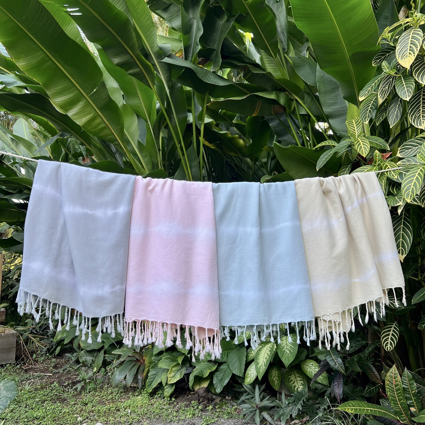 Four colorful towels hanging against a green leafy background