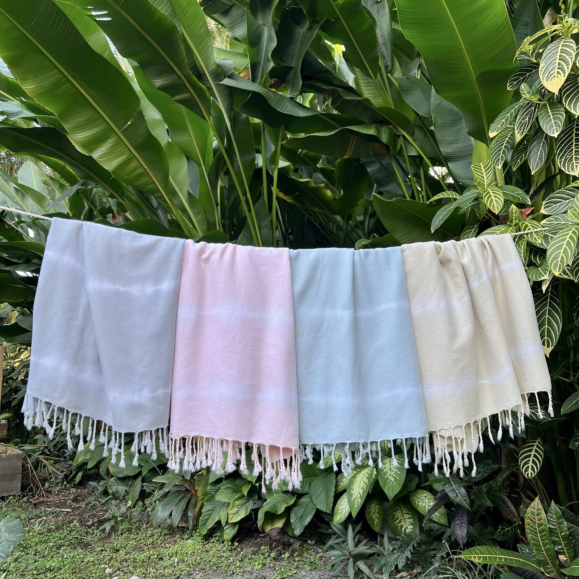 Four colorful towels hanging against a green leafy background
