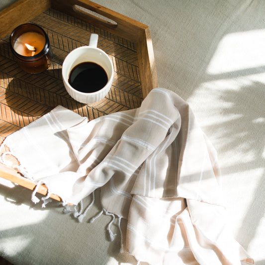 Wooden tray with a cup of coffee, candle, and white towel on a light surface.